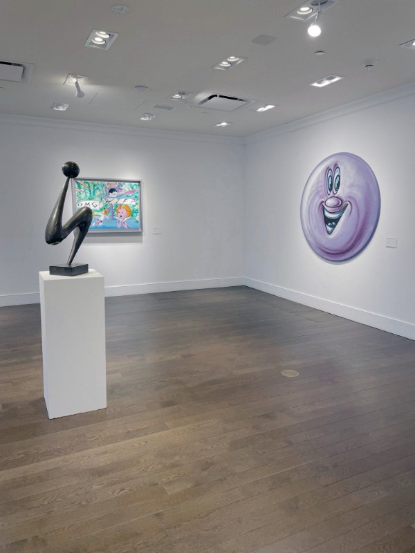 Works by Kenny Scharf, including a large round smiling-face canvas, in a gallery installation